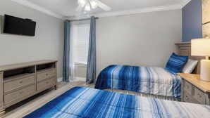 Une chambre avec deux lits, un ventilateur de plafond, une télévision et une commode.