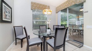 A dining area with a glass table, four chairs, a hanging light fixture, and a window with blinds. - Windsor Hills Resort/2 Miles Disney/Private Pool and Hot Tub/Games Room/FreeWifi (Kissimmee)