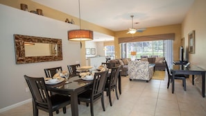 A dining area with a table set for four, surrounded by chairs. There is a sofa and a television in the background. - Orange Blossom Villa (Kissimmee)
