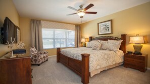 A bedroom with a bed, a ceiling fan, a window with blinds, a chair, a bedside table with a lamp, and a framed picture on the wall. - Windsor Hills Resort/2 Miles Disney/Private Pool and Hot Tub/Games Room/FreeWifi (Kissimmee)