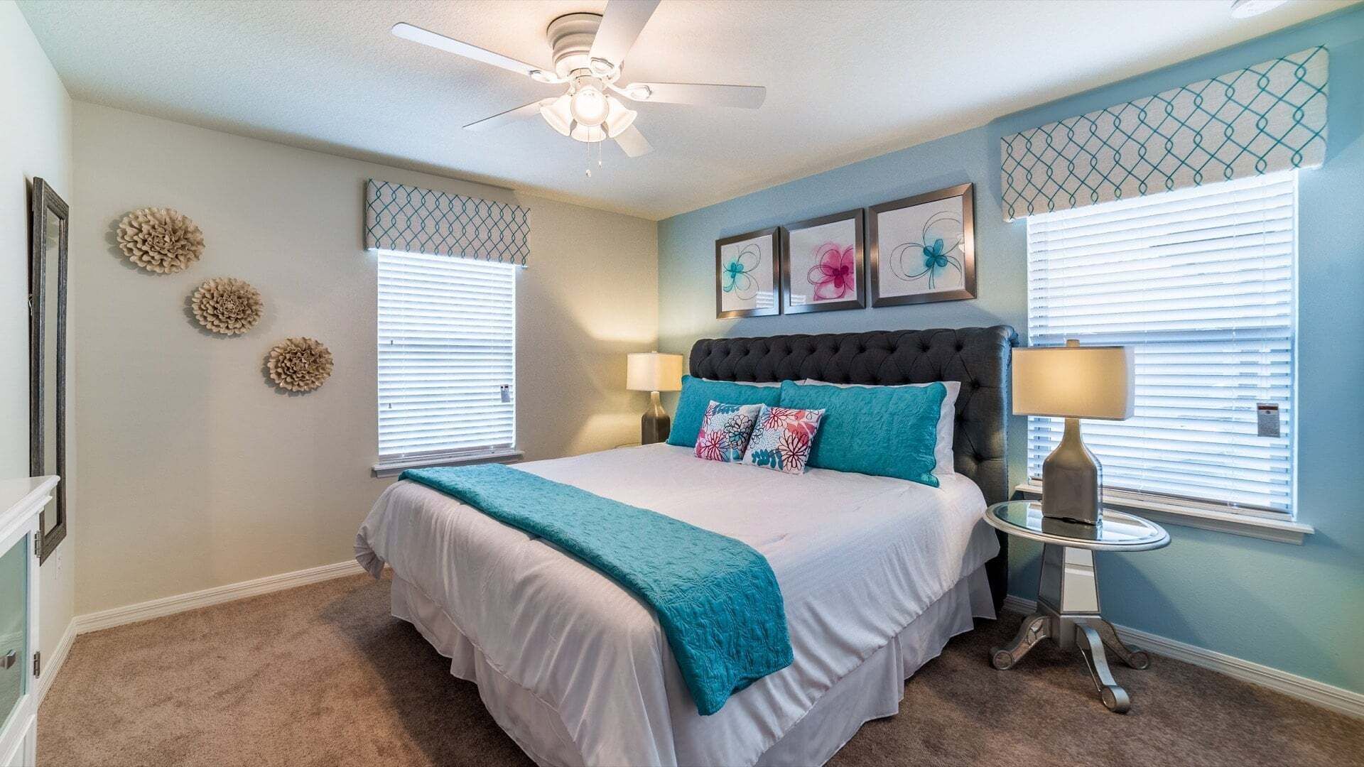 A bedroom with a bed, two wall-mounted lamps, a ceiling fan, and decorative wall art.