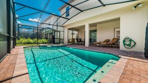Piscina com teto de vidro, rodeada por um espaço de estar com cadeiras e uma mangueira.