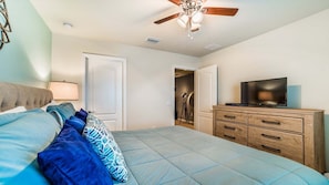Ein Schlafzimmer mit Bett, Deckenventilator, Fernseher und Kommode.