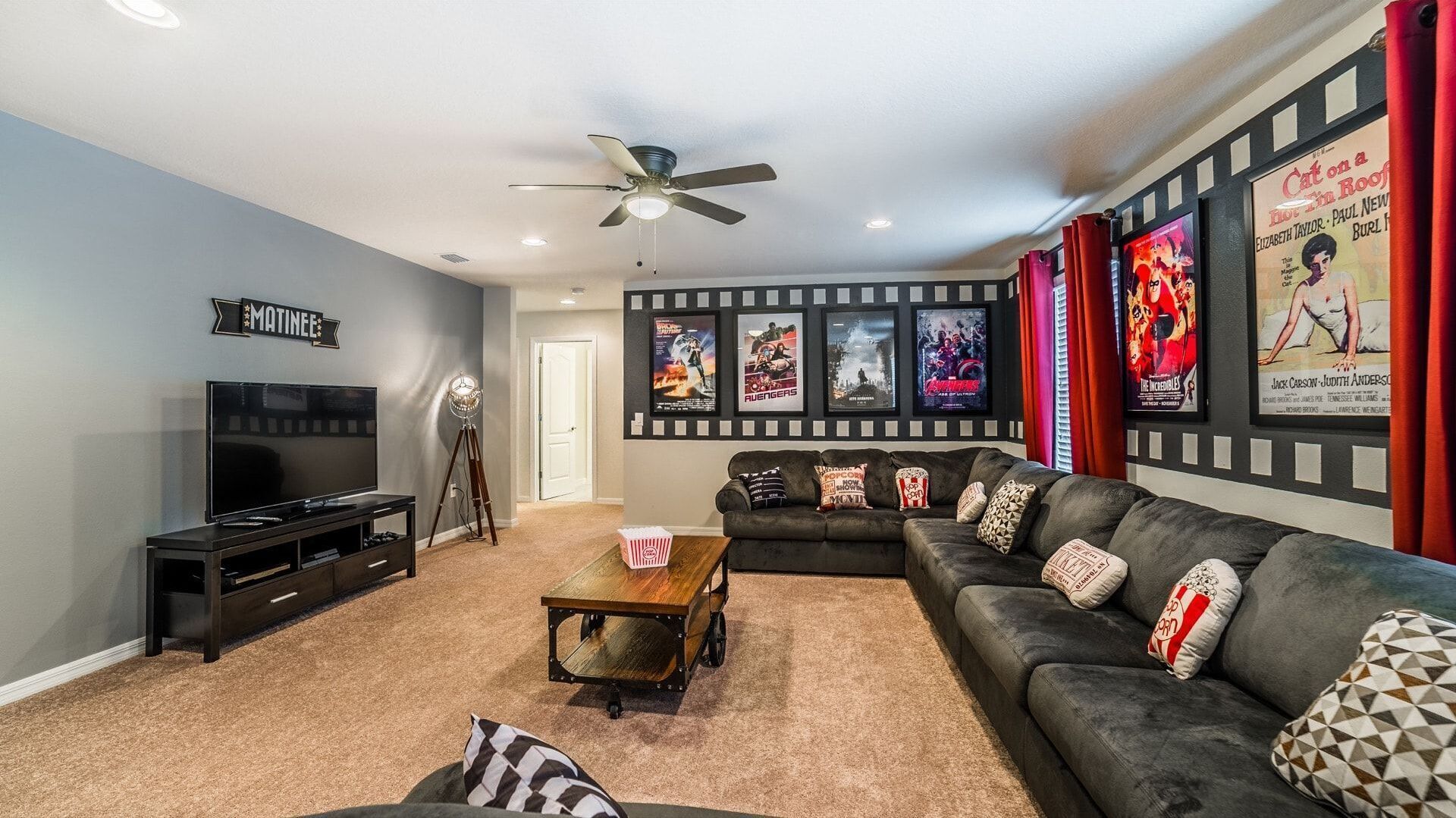 Ein Wohnzimmer mit Fernseher, Deckenventilator, Popcorntisch, einer Couch und Filmplakaten an der Wand.