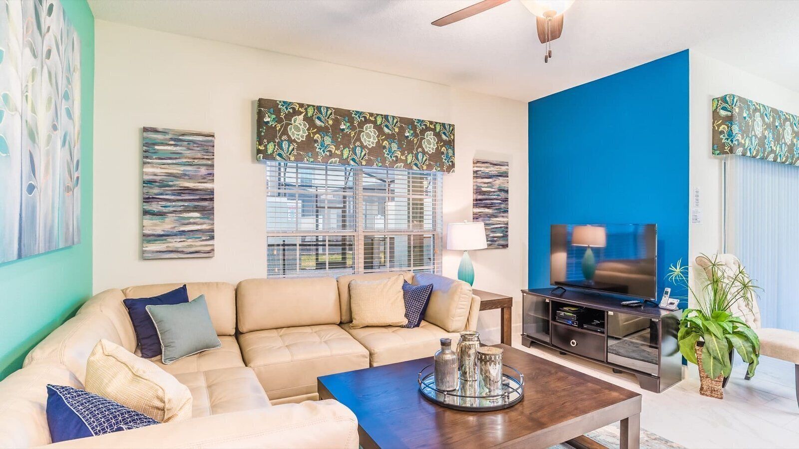 A living room with a beige sectional sofa, a coffee table with decorative items, a television on a black stand, and a blue accent wall.