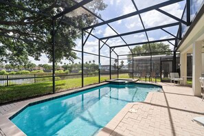 Ein Schwimmbad mit Glasverkleidung, umgeben von einer Ziegelterrasse und Gartenmöbeln.