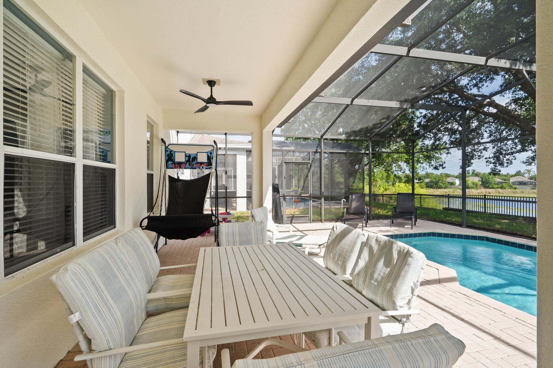 A covered outdoor area with a pool, a ceiling fan, and a swing chair.