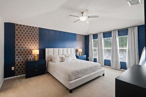 Ein Schlafzimmer mit einem Bett, Nachttischen, einem Deckenventilator und einem Fenster mit Vorhängen.