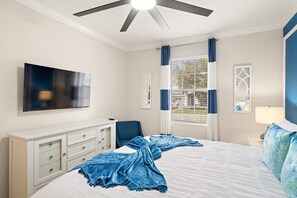 Um quarto com uma cama, televisão, escrivaninha e janela com cortinas.