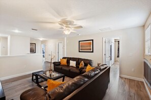 A spacious living room with a dark leather sofa, a glass coffee table, and a ceiling fan. - The Grand Slam - Eight Bedroom Apartment, Sleeps 19 (Kissimmee)