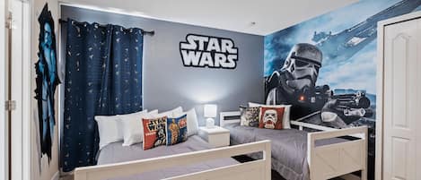 Une chambre avec un mur décoré sur le thème de Star Wars, deux lits et une armoire.