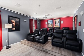 A home theater room with a red wall, black leather recliners, a ceiling projector, and framed movie posters. - The Grand Slam - Eight Bedroom Apartment, Sleeps 19 (Kissimmee)