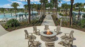 A circular outdoor seating area with a fire pit surrounded by Adirondack chairs, a pathway leading to a pool, and palm trees. - The Forever Home - Five Bedroom House, Sleeps 12 (Kissimmee)