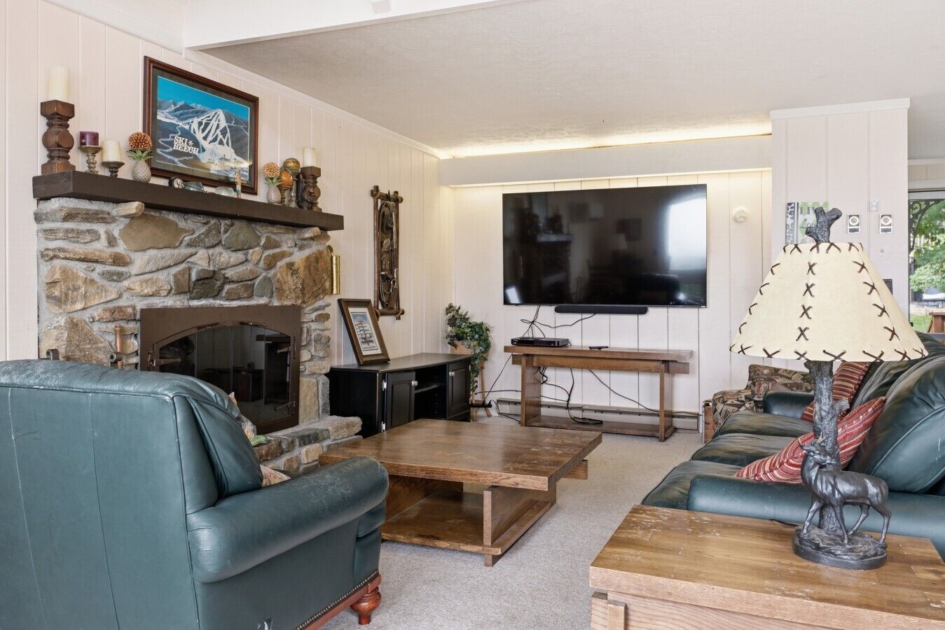 Un salon avec une cheminée en pierre, un téléviseur à écran plat, des canapés en cuir et une table basse en bois.