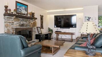 Un salon avec une cheminée en pierre, un téléviseur à écran plat, des canapés en cuir et une table basse en bois.