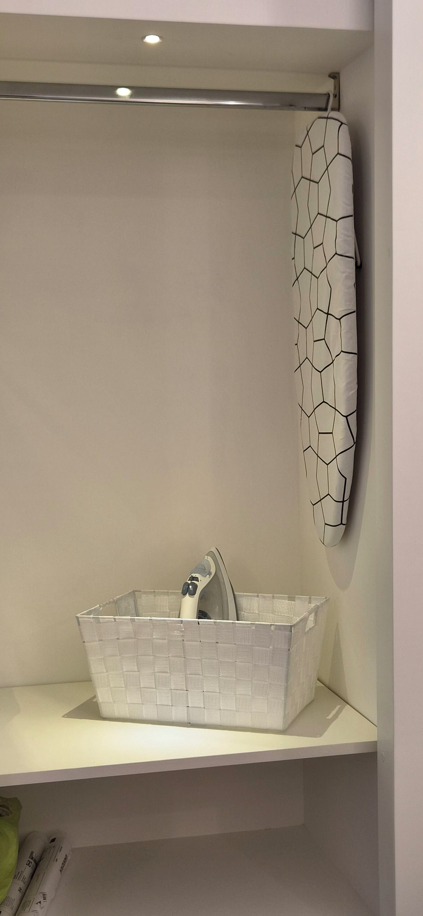 Un baño con un estante blanco, una cesta blanca y un perchero blanco con diseño geométrico.