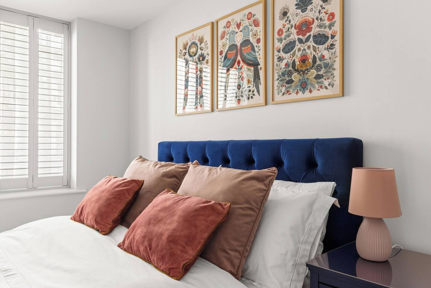 Une chambre à coucher avec un lit, des oreillers, une table de chevet, une lampe et des œuvres d’art murales.