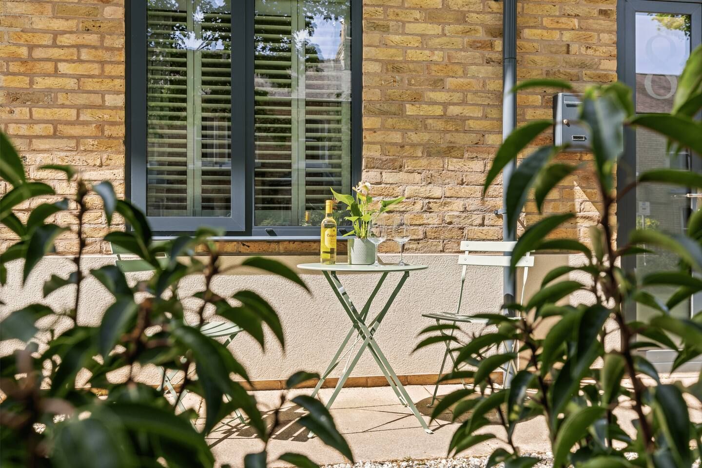 A brick building with a window and a small table with a bottle and a glass.