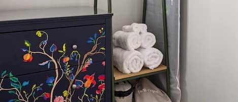 A room with a dark-colored dresser with floral designs, a green metal drying rack with towels, and a grey curtain.