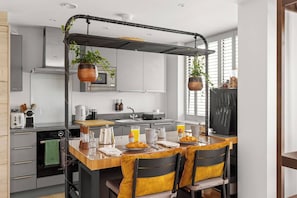 A modern kitchen with a central island, a hanging plant, and a dining area with chairs. - The Bee Apartment & Patio, St John's Mews, 10-Minutes Walk From The York Minster (York)