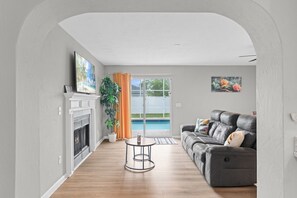 Ein Wohnzimmer mit Kamin, einer Couch, einem Fernseher und Blick auf einen Pool durch Glastüren.