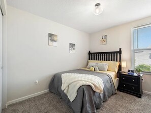 Une chambre à coucher comprenant un lit, une table de chevet, des œuvres d’art murales et une fenêtre avec des stores.