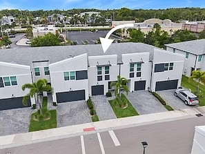 A modern residential building with multiple garage doors, a parking lot, and a clear sky. - Snowbird Special: Mint 3BR Gated Townhome, Seasonal Stay Available (Stuart)