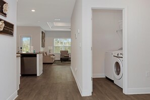 Ein Waschraum mit Waschmaschine und Trockner, eine Küchenzeile mit Geschirrspüler sowie ein Wohnzimmer mit Sofa und Couchtisch.