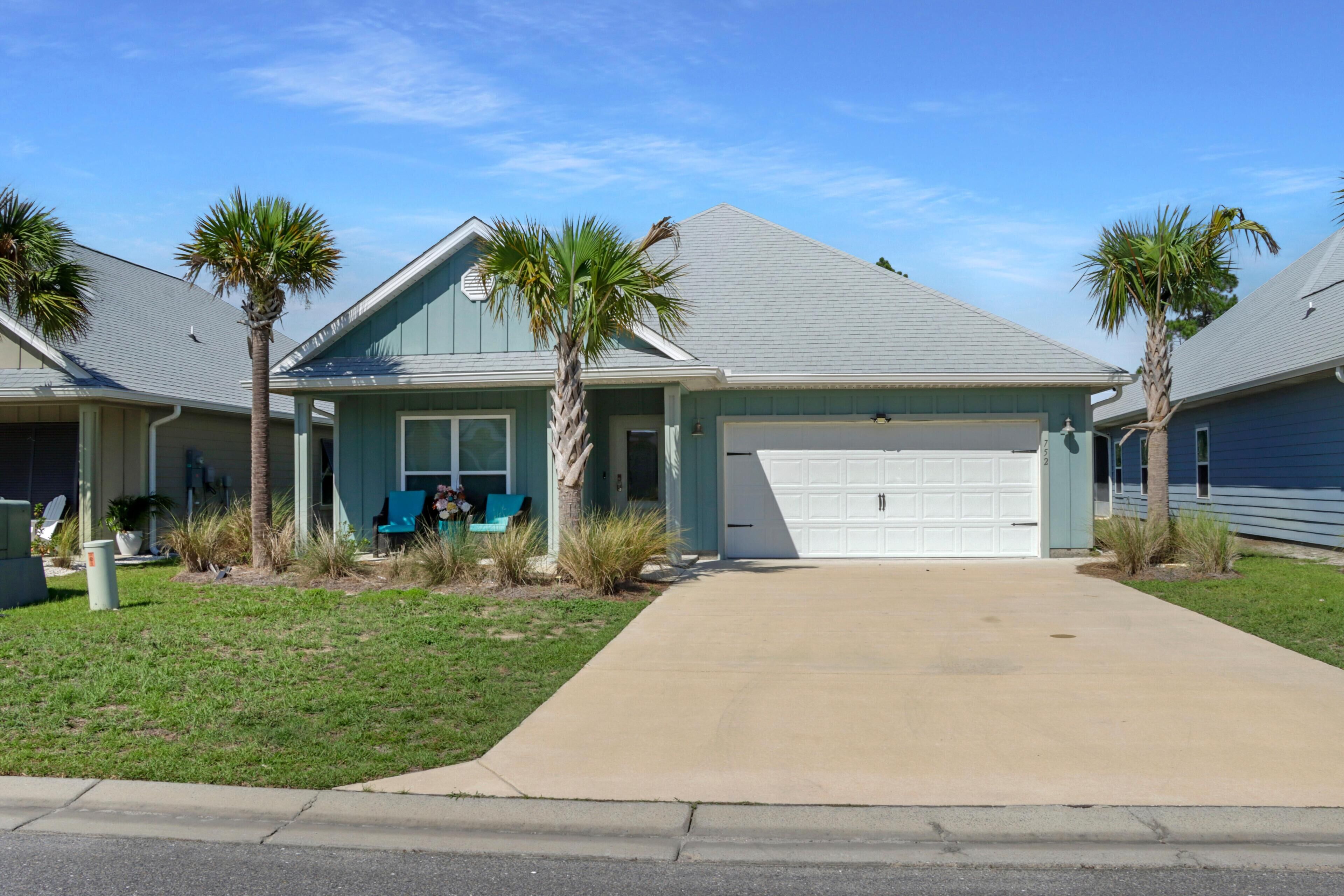 A residential house with a garage, a driveway, and a lawn with palm trees.