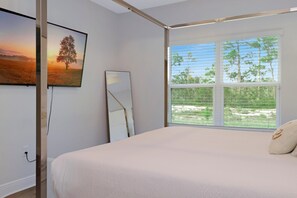 Ein Schlafzimmer mit großem Fenster, einem Bett, einem Spiegel und einem Bild an der Wand.