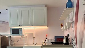 Et køkken med hvide skabe, en mikrobølgeovn, en vask og en hylde med service.