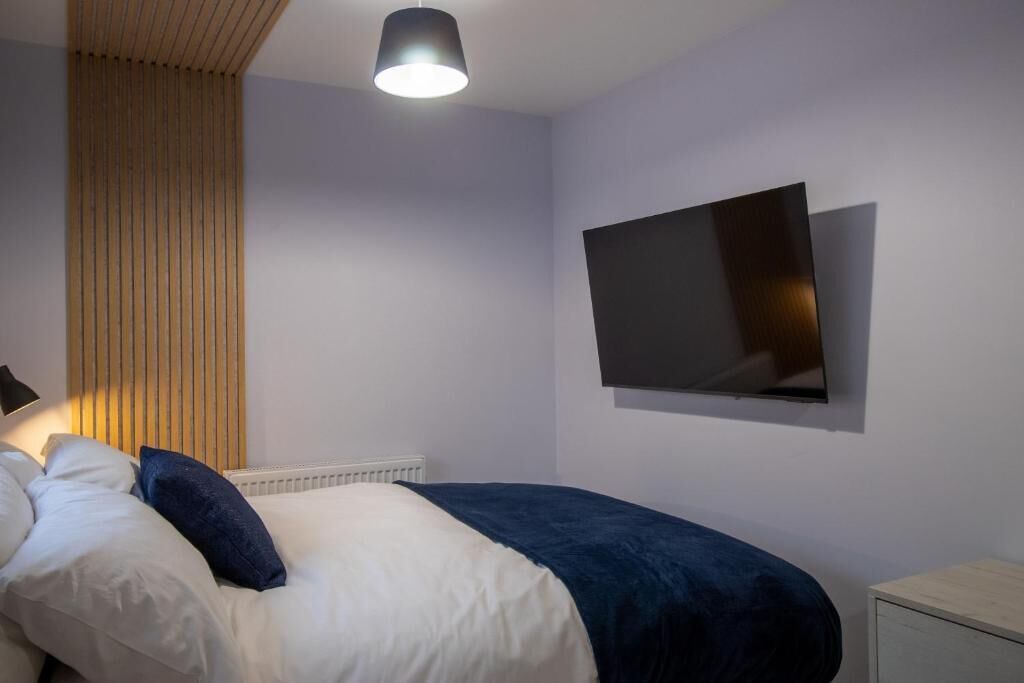 A bedroom with a bed, a wall-mounted TV, and a bedside table.