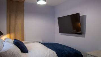 A bedroom with a bed, a wall-mounted TV, and a bedside table.