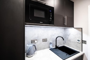 Una cocina moderna con microondas integrado, hervidor y pileta.