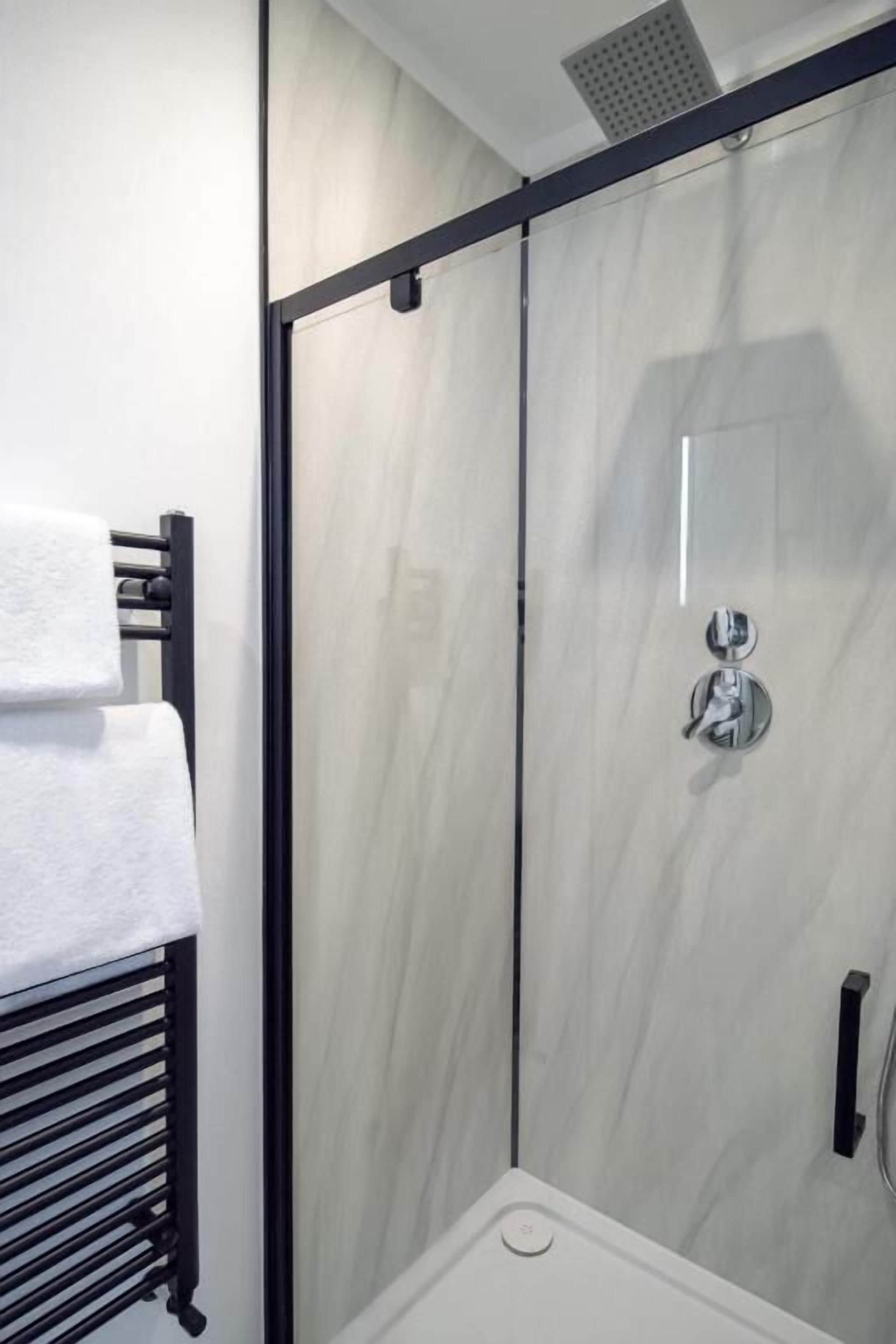 Un baño moderno con cabina de ducha de vidrio, un perchero y panel de control de la ducha a la vista.