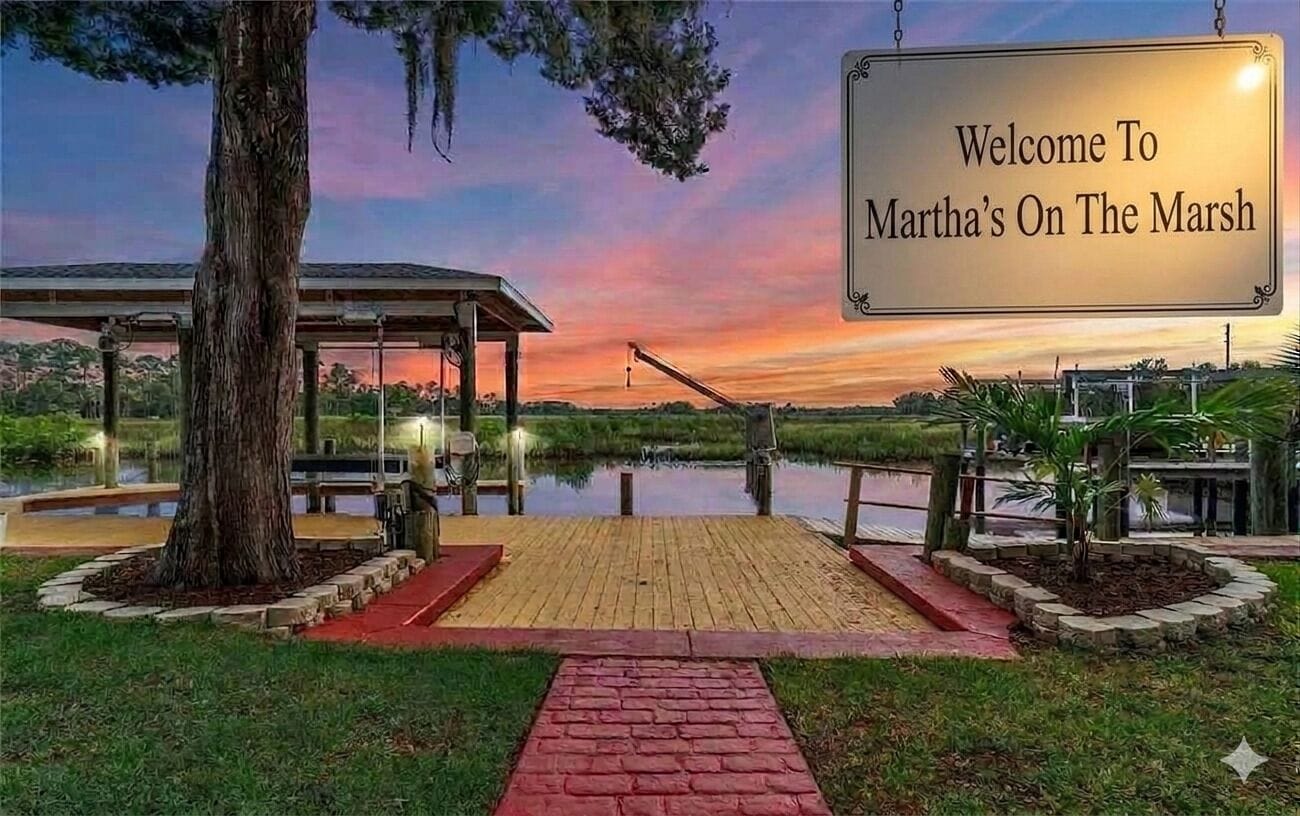 A wooden dock leading to a covered pavilion with a sign reading 'Welcome To Martha's On The Marsh.'