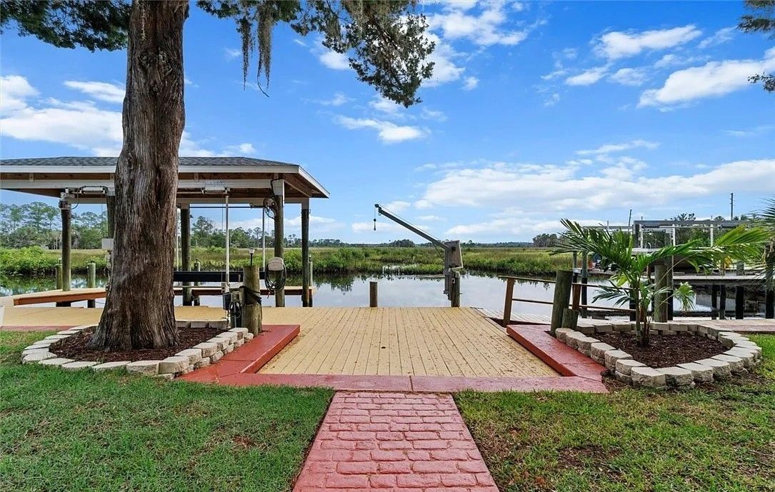 A gazebo with a wooden deck, a pond, and a clear sky.
