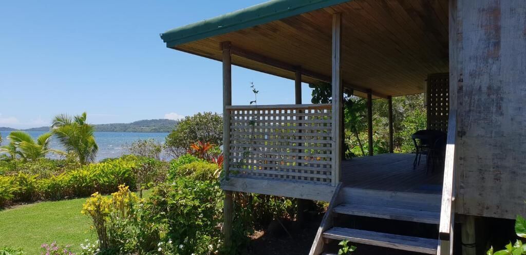 Een overdekt buitengebied met uitzicht op zee, een houten terras en een zithoek.
