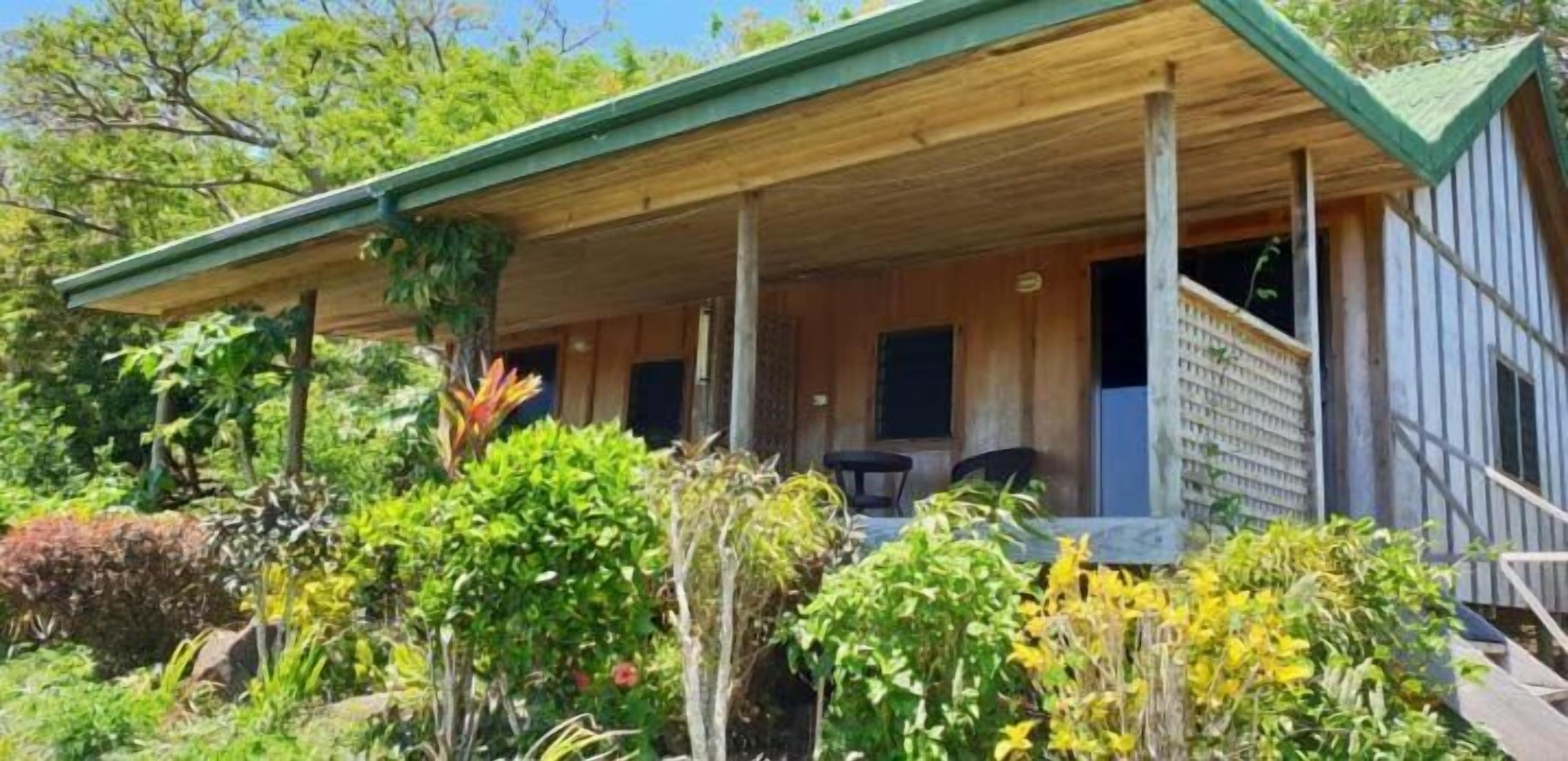 A wooden cabin with a covered porch, surrounded by lush greenery.