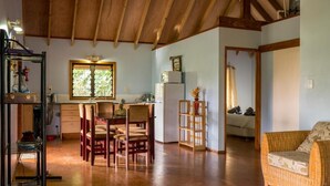 A spacious living area with a wooden ceiling, a dining table with chairs, a kitchen area with a refrigerator, and a cozy seating area with a sofa.