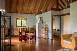 A spacious living area with a wooden ceiling, a dining table with chairs, a kitchen area with a refrigerator, and a cozy seating area with a sofa.