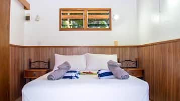 A hotel room with a wooden paneled wall, a bed with white linens, two bedside tables, and a window with wooden shutters.