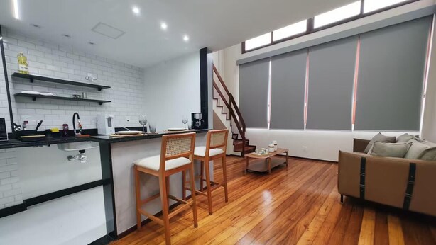 Una cucina moderna con piastrelle bianche a metro, sedie e tavolo da pranzo in legno, e una scala che conduce a un balcone.