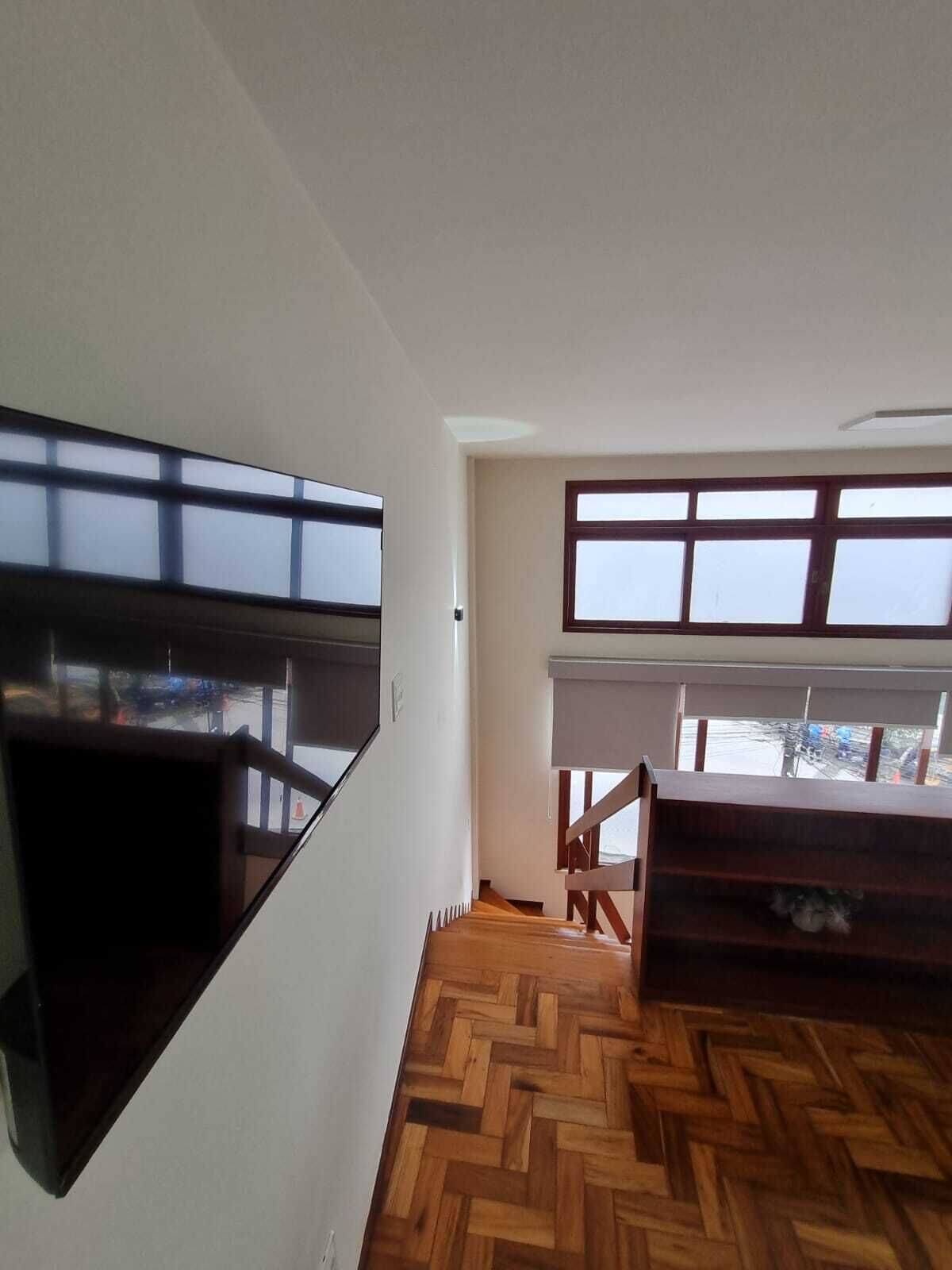 A room with a herringbone-patterned wooden floor, a large window with blinds, and a built-in wooden shelf.
