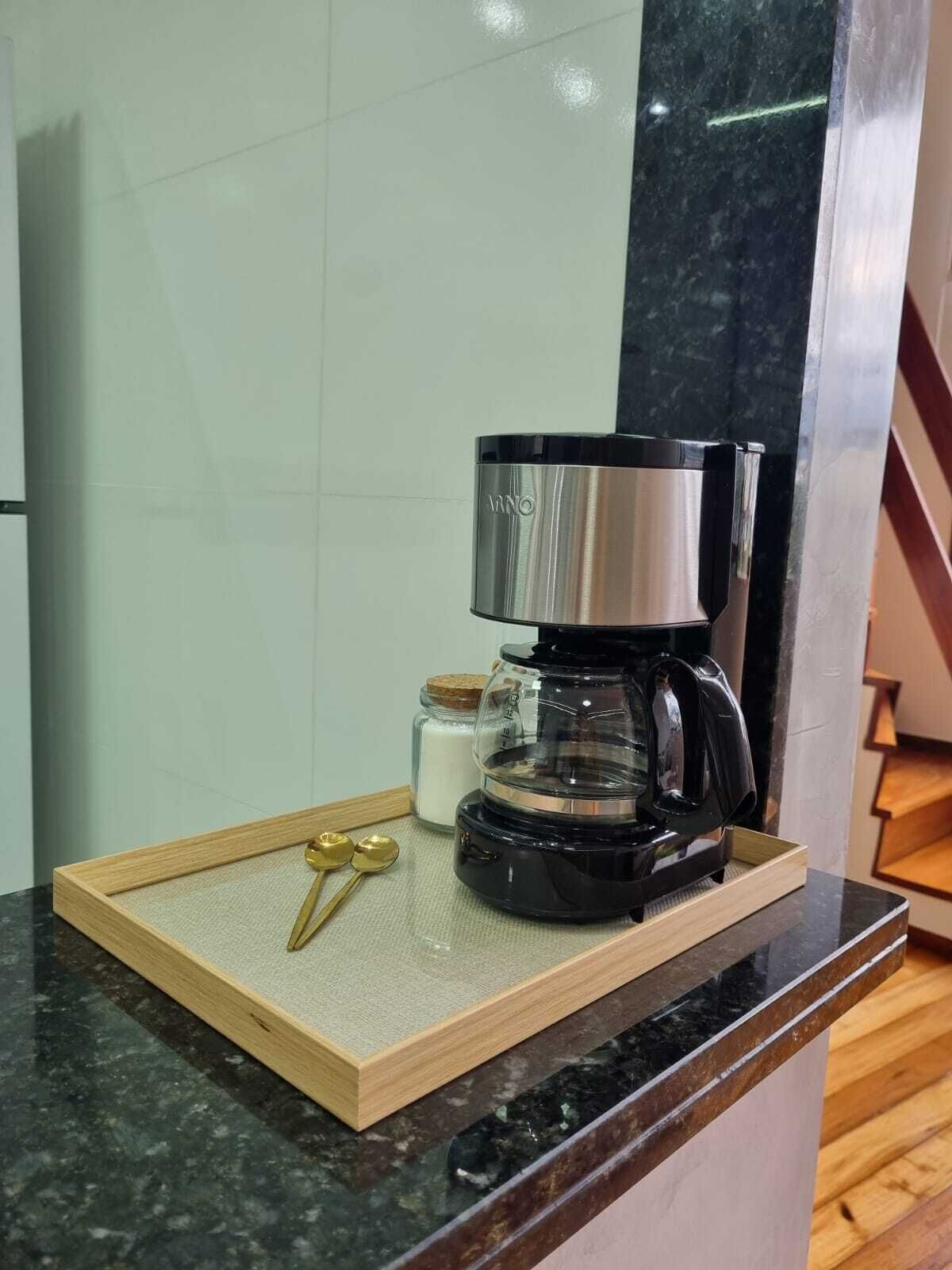 Eine Kaffeemaschine auf einem Holztablett mit einer Marmarausziehtafel, ein Zuckerbehälter und zwei goldene Löffel.