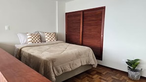 A bedroom with a bed, a wooden wardrobe, a potted plant, and a wooden bench. - Loft Fátima (Teresópolis)