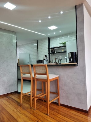 A modern kitchen with white brick backsplash, wooden chairs, and a large mirror reflecting the space.
