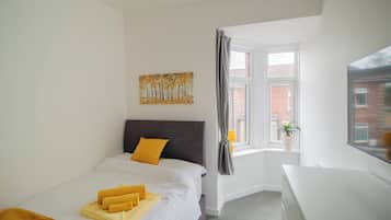 A bedroom with a bed, a desk, a window, and a painting on the wall.