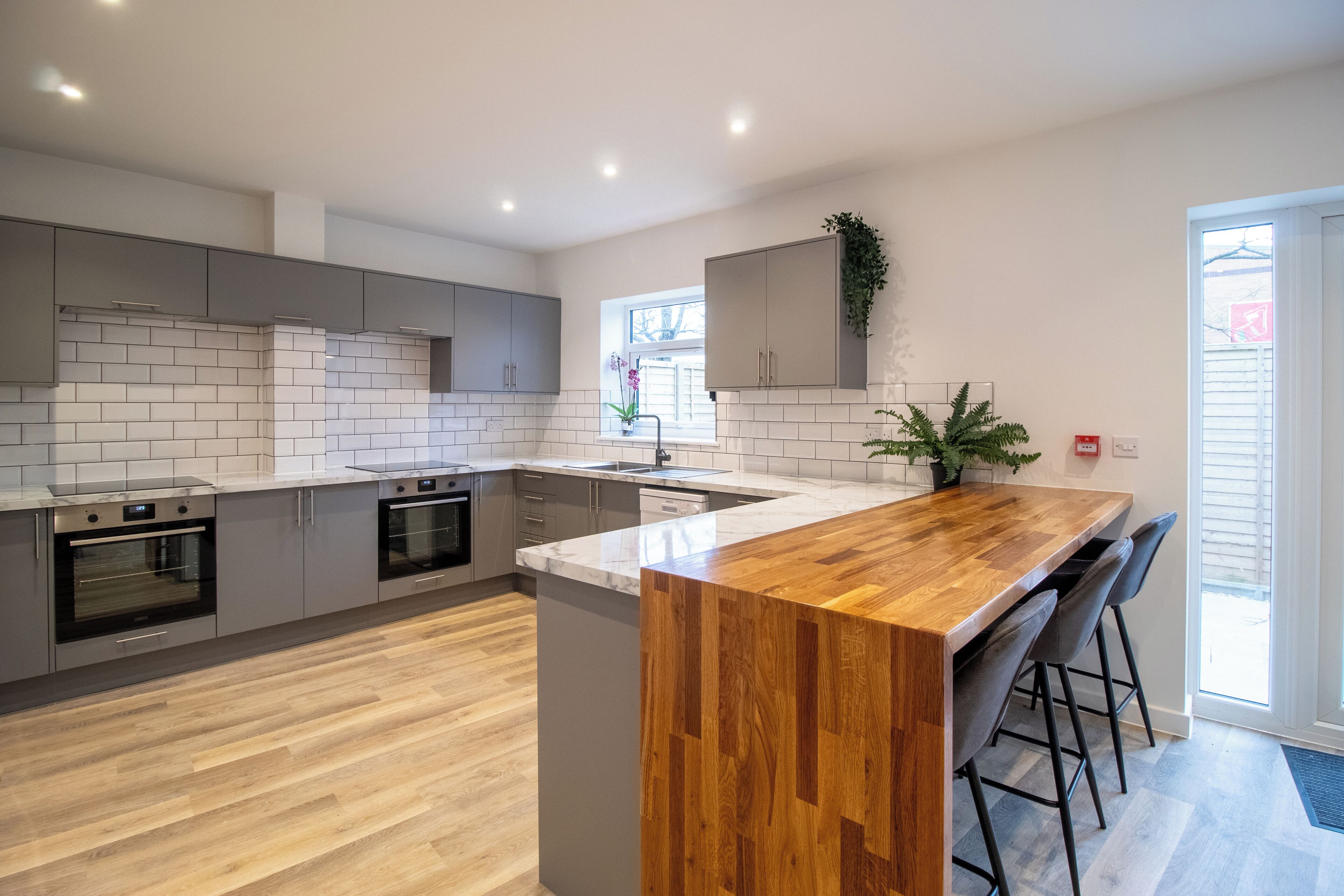 A modern kitchen with grey cabinets, a wooden island, and a built-in oven.