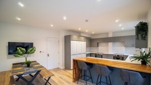 A modern kitchen with a wooden island, bar stools, and a dining table with a unique design. - 29 Twyford (Eastleigh)